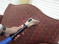 Two cleaning people are cleaning the inside of a classroom by wiping down desks and using a microfiber mop to wipe dust and debris off floors