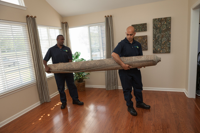 two men carrying a large rolled up rug